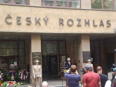 Před budovou s nápisem „ČESKÝ ROZHLAS“ stojí lidé a účastníci ceremonie u vchodu.