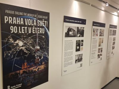 Výstava v galerii: velký plakát „Praha volá svět!“ a řada informačních panelů na stěně.