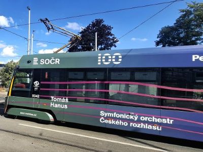 Čelní pohled na tramvaj s nápisem „100“ a „Symfonický orchestr“ na modrém pozadí oblohy.