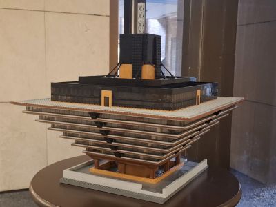 Model budovy s vícevrstvou konstrukcí a schodišti, umístěný na podstavci v interiéru.