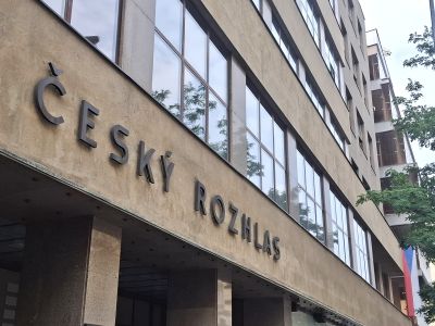 Nápis „Ceský rozhlas“ na fasádě budovy s řadami oken a stromy vedle.