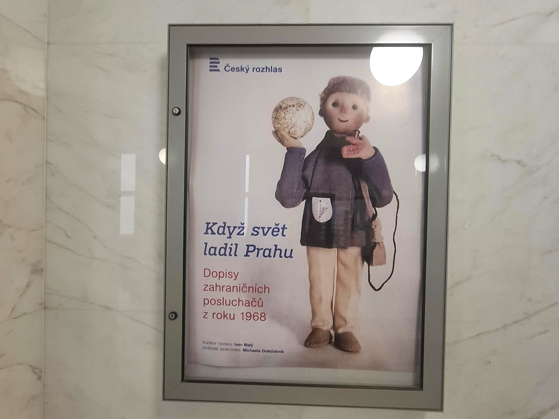 Výstavní plakát Český rozhlas s loutkou držící mikrofon a textem Když svět ladí Prahu.