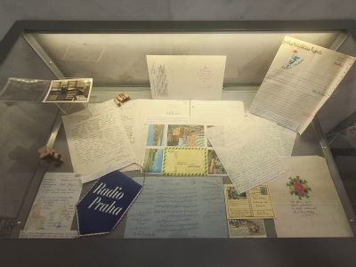 Skleněná vitrína s hromadou historických dokumentů, dopisů a fotografií, včetně knihy Radio Praha.