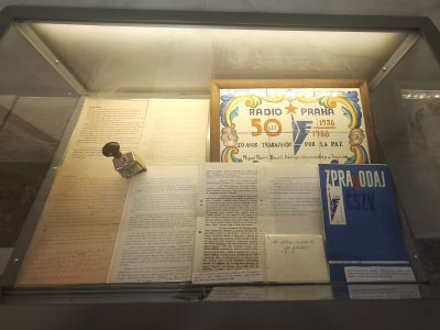 Vitrína s dobovými dokumenty, novinami a plakátem „Radio Praha 1936“ na pozadí.