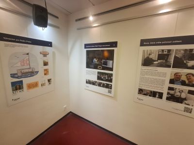Interiér výstavní místnosti s několika informačními panely a fotografiemi na bílých stěnách.